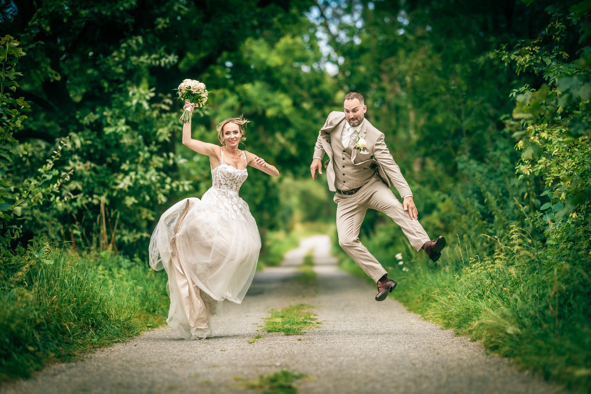 Veselá svatební momentka – novomanželé ve výskoku na lesní cestě